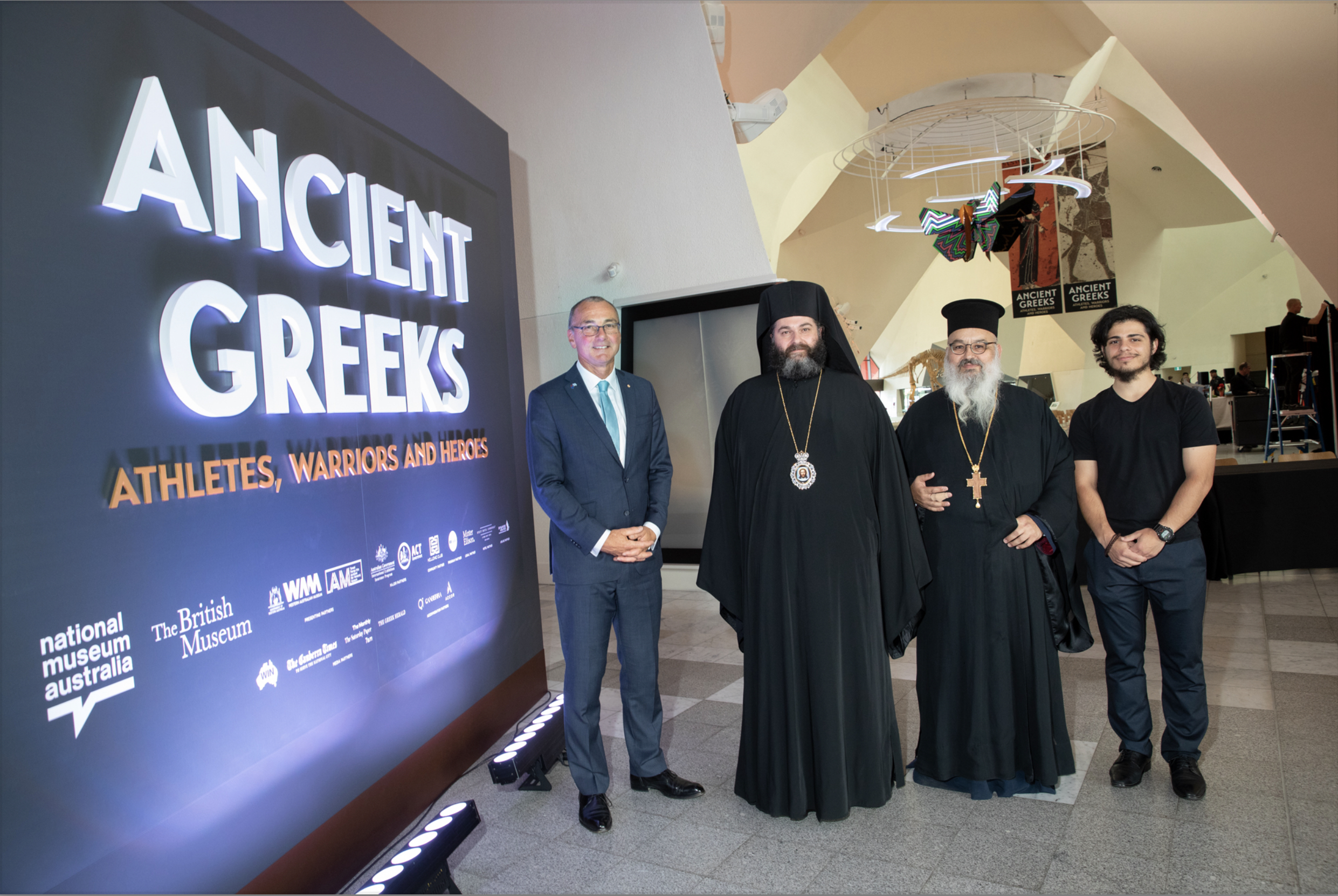 A picture of men in front of the Ancient Greeks, Athletes, Warriors and Heroes sign at the exhibit