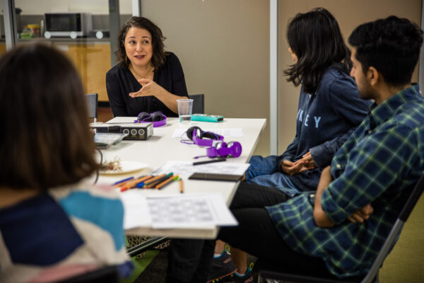 Image description: CEO of Diversity Arts Lena Nahlous speaking to a table full of young diverse artists who participated in the StoryCasters program